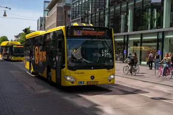 Martijn Stoof Un autobus di trasporto pubblico di colore giallo brillante su una strada cittadina trafficata, con ciclisti e pedoni.